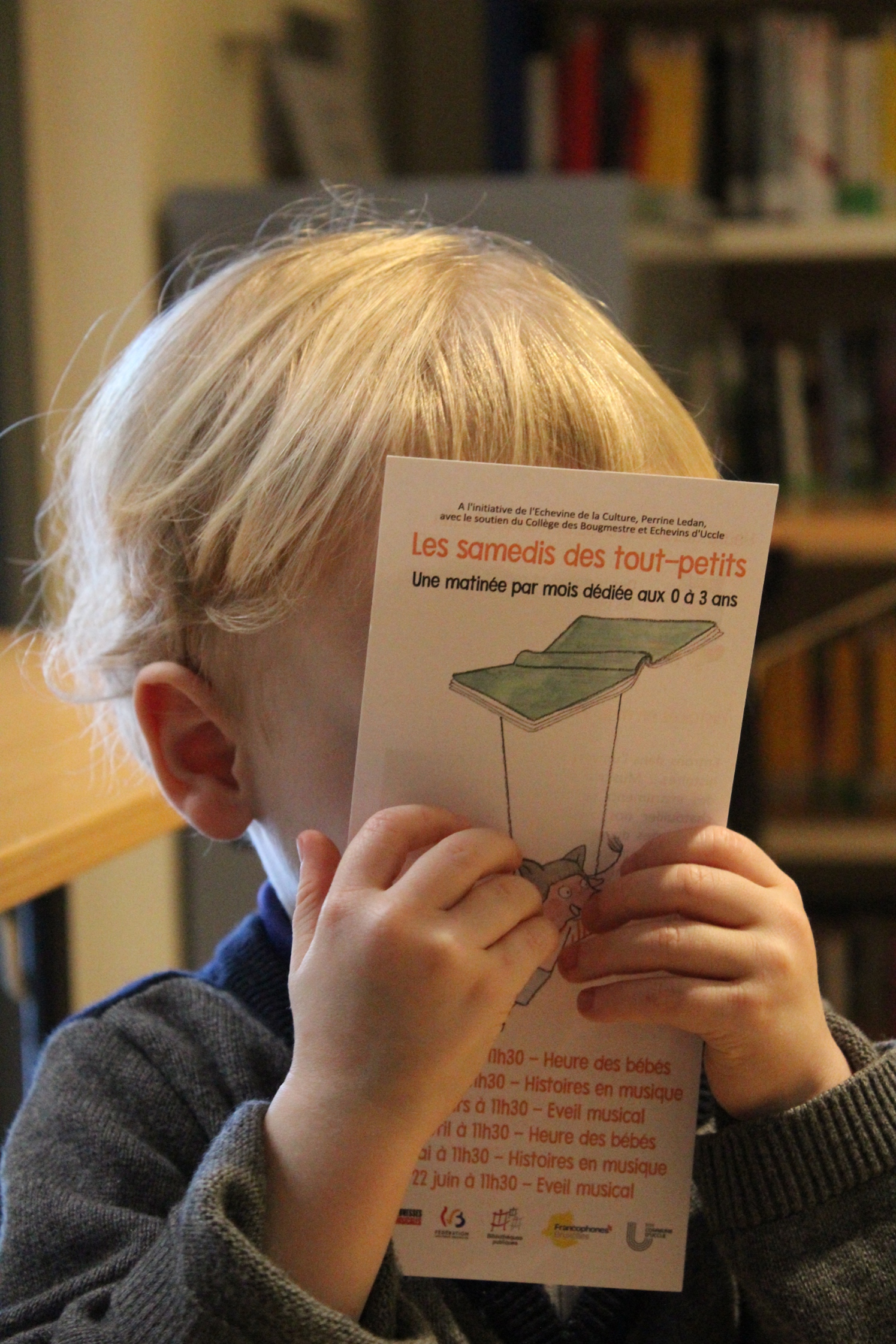 Bébé tenant un flyer des animations bébés devant son visage